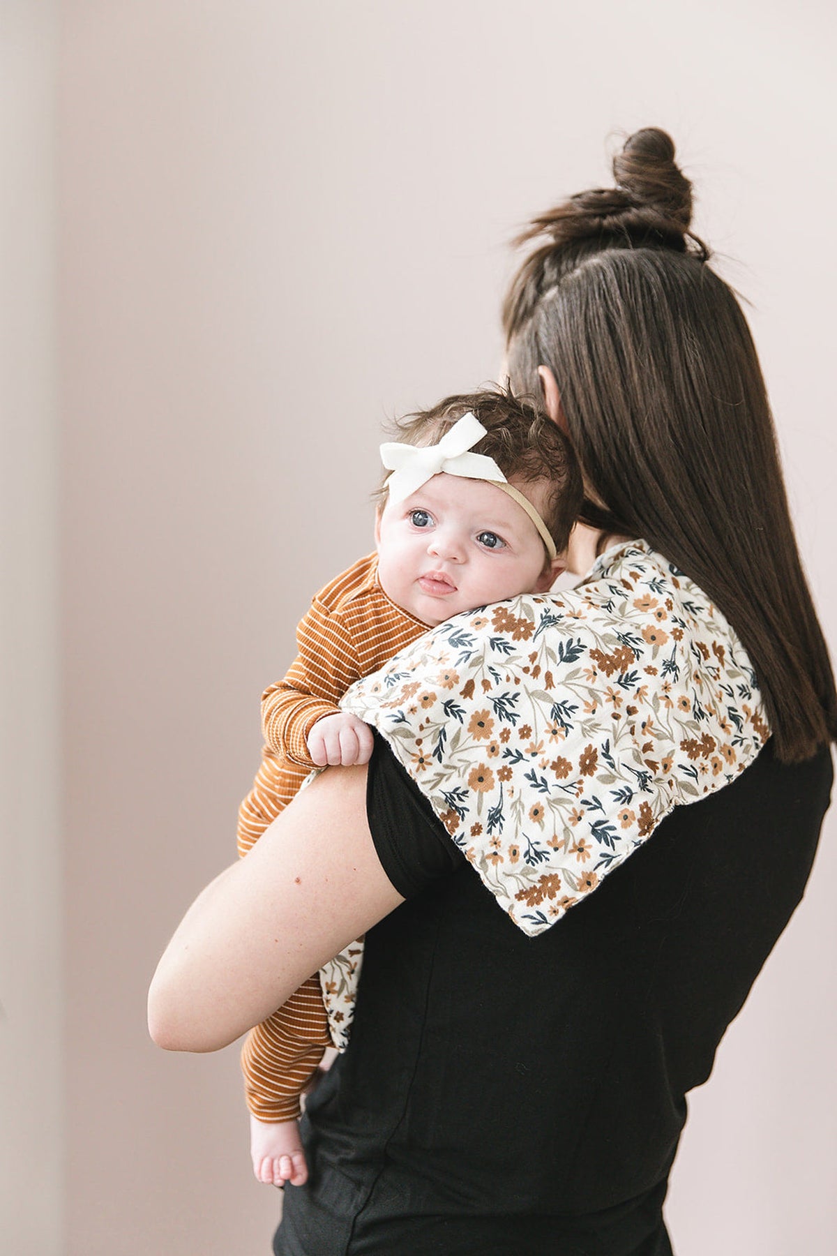 A woman holds a baby on her shoulder, using a floral muslin burp cloth.