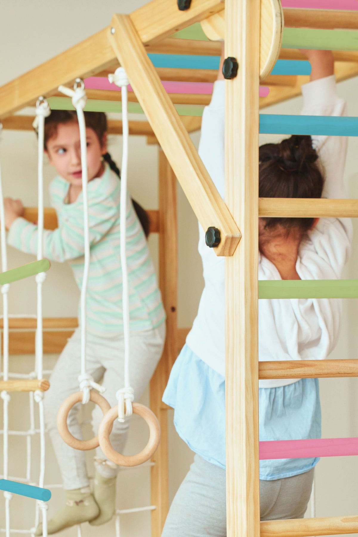 Two children play on a wooden foldable jungle gym featuring colorful bars and climbing elements. The structure is designed for indoor use, promoting active play and coordination.