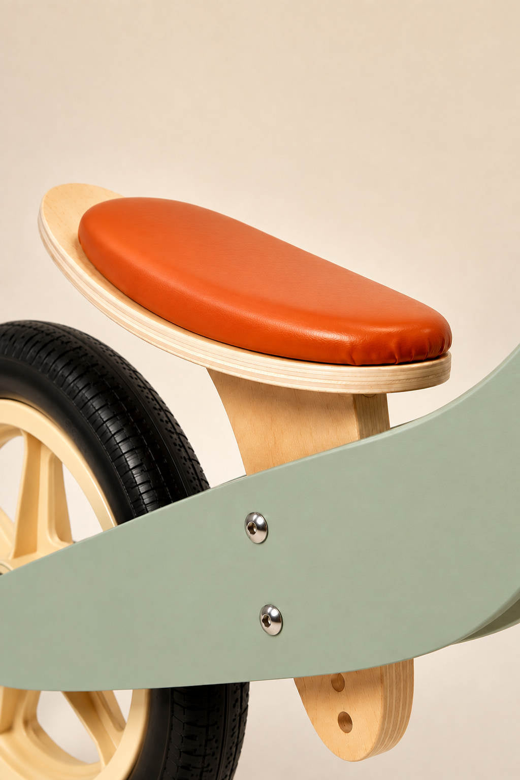 Close-up of a wooden balance bike featuring a mint green frame and a brown padded seat. The design emphasizes sustainable materials, suitable for children aged 3 to 5.