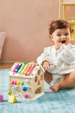 A toddler sits on a blue rug, engaging with a colorful wooden activity cube featuring various interactive elements.