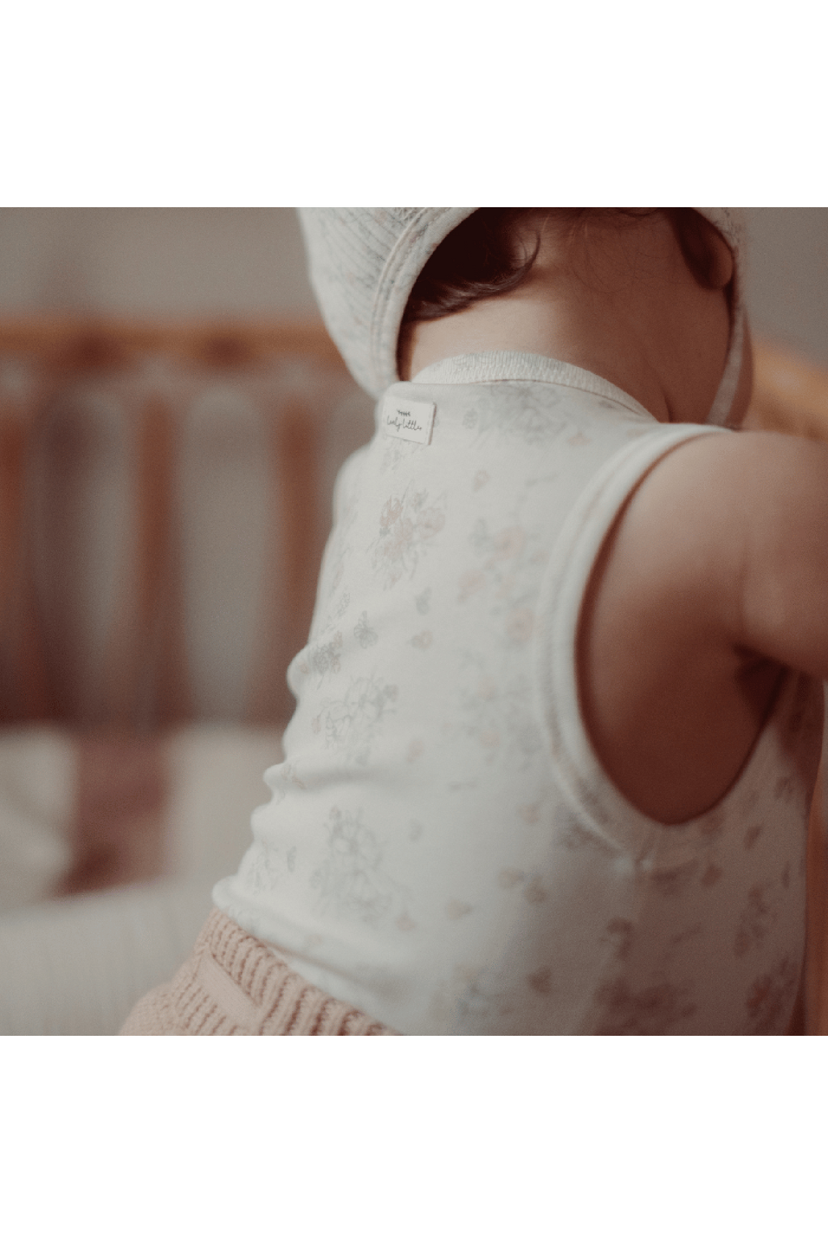 A baby is wearing a soft, floral-printed cotton tank top with a delicate neckline. The cozy setting features warm tones, emphasizing the tanks comfortable and stylish design for toddlers.