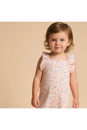 A young child smiles while wearing a floral-patterned romper with delicate flutter sleeves. The soft, pastel colors and organic cotton material highlight its playful and comfortable design.