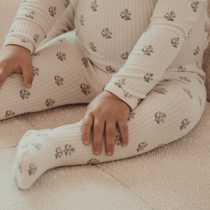 A child sits on a soft surface, wearing a light-colored outfit with subtle floral patterns. The fabric appears soft and comfortable, suitable for everyday wear.