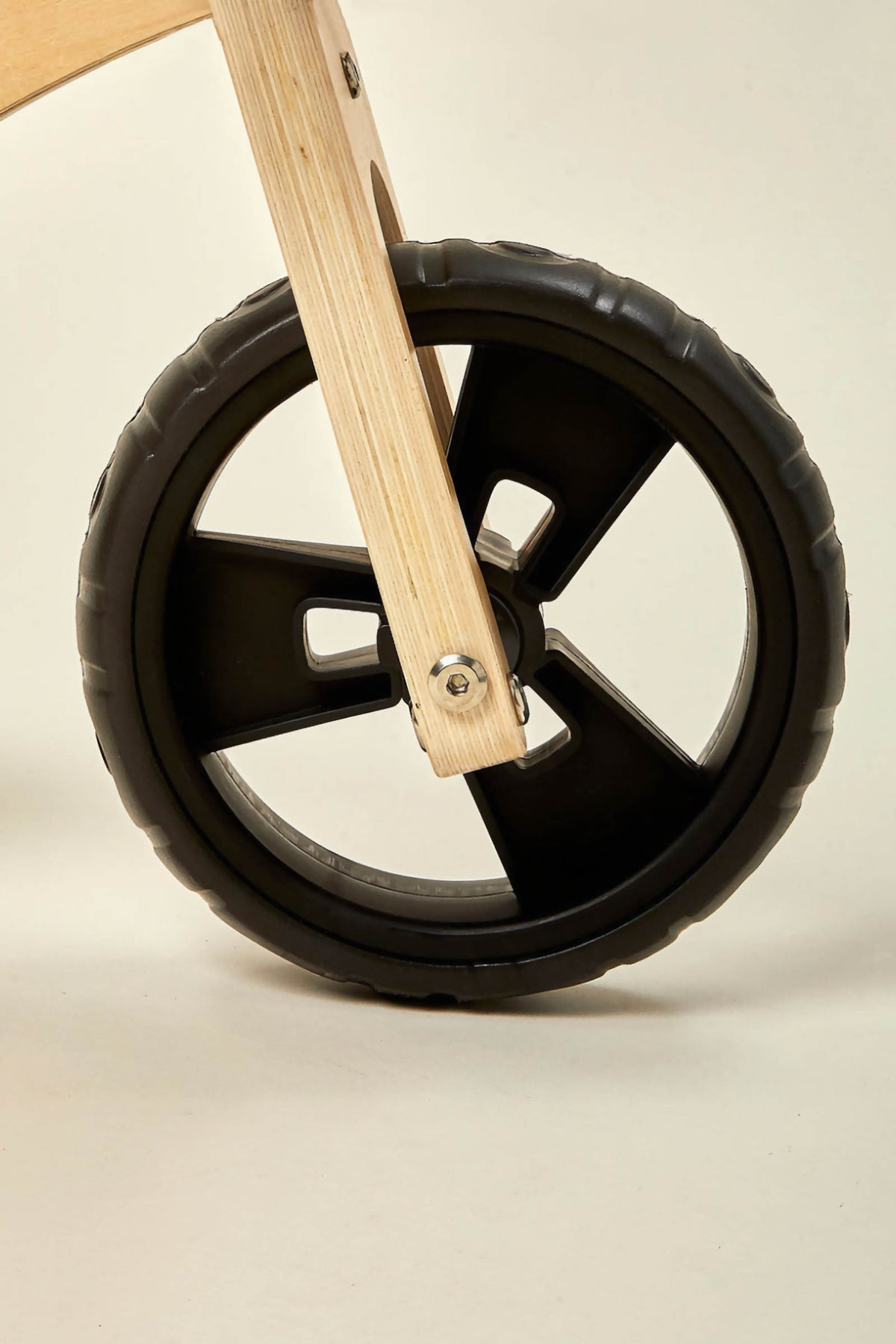 Close-up of a black rubber wheel attached to a mini wooden balance bike, showcasing its sturdy design and smooth rolling capability, ideal for toddlers aged 18 months to 3 years.