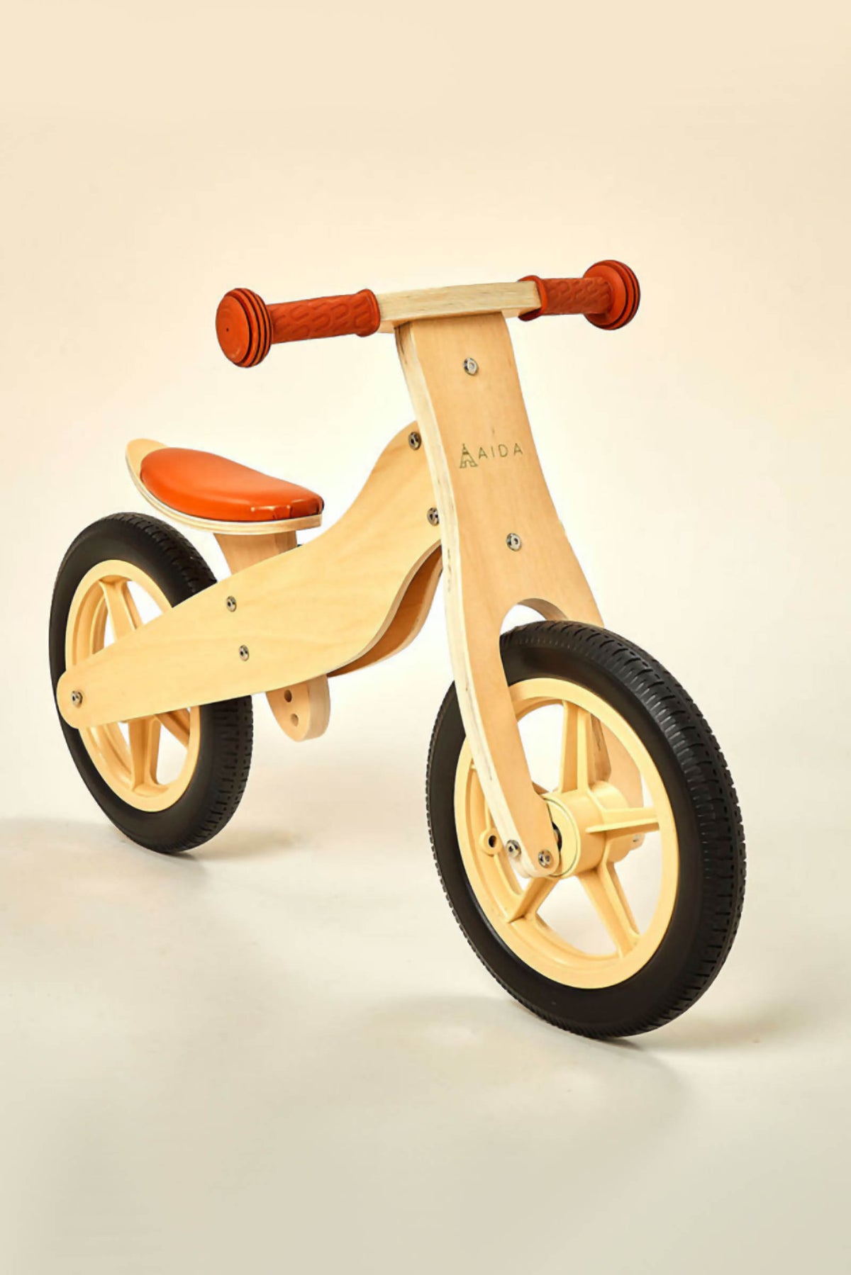 A natural wooden balance bike features a minimalist design with an orange seat and rubber tires.