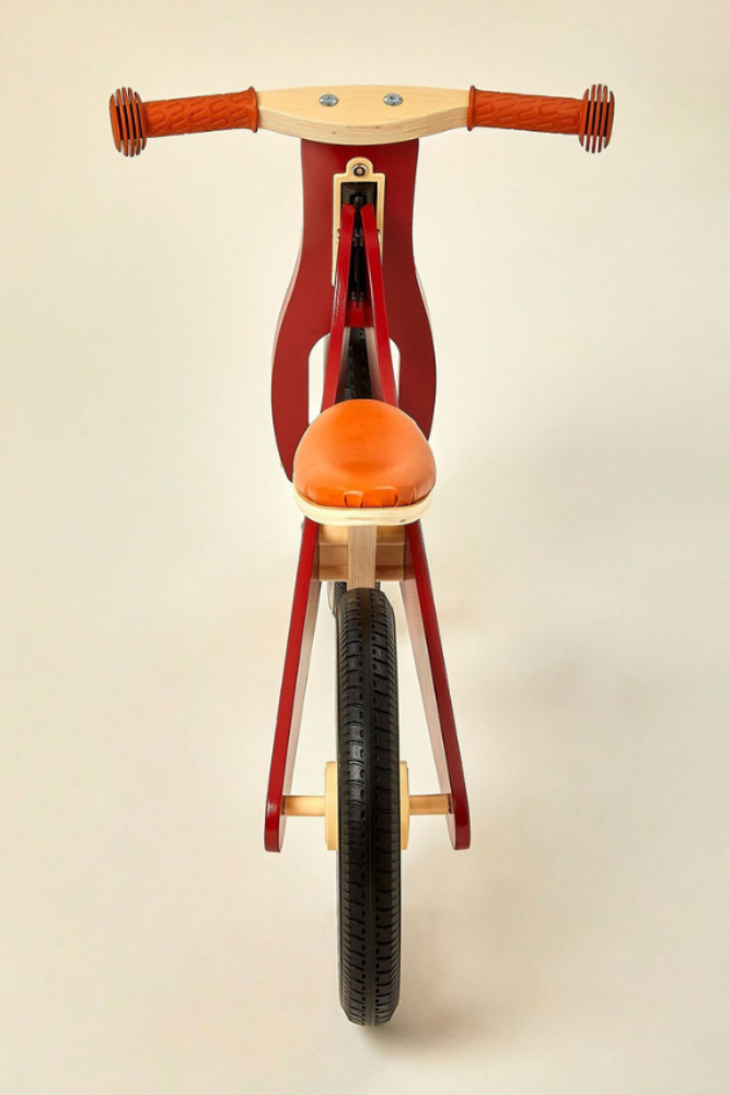 A front view of a red wooden balance bike featuring an orange seat and brown handlebars.