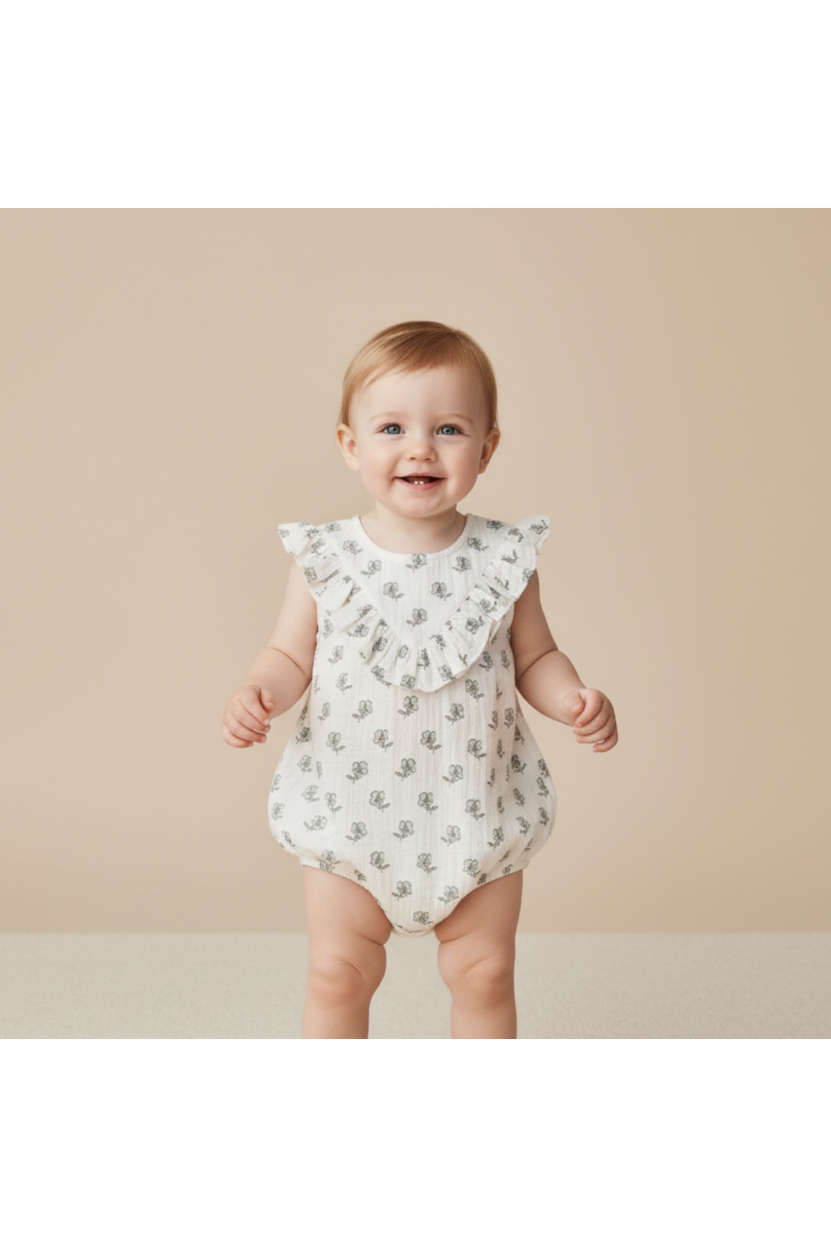 A smiling baby wears a sleeveless, organic cotton bubble romper with ruffled shoulders and a whimsical pattern. The soft fabric is perfect for playtime, set against a neutral background.