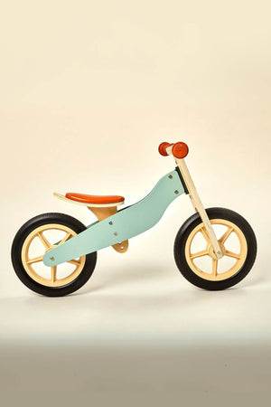 A wooden balance bike features a light blue frame, orange seat, and black wheels, designed for children ages 2 to 4.