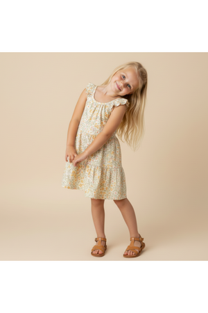 A young girl poses in a light yellow, organic cotton ruffle tiered dress adorned with delicate floral patterns.