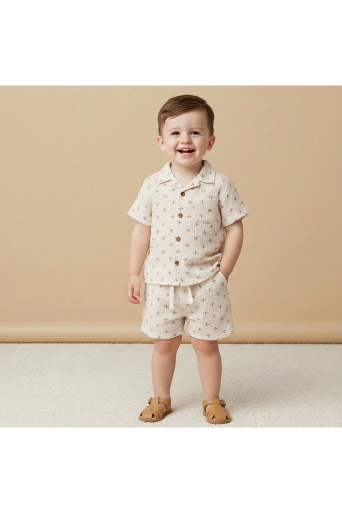 A smiling young boy stands in a lightweight, cream-colored organic cotton shirt and shorts set featuring a subtle star pattern. The outfit is perfect for summer adventures and playful outings.
