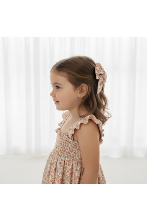 A young girl with a charming smile is wearing a floral dress and an organic Sienna hair bow clip.