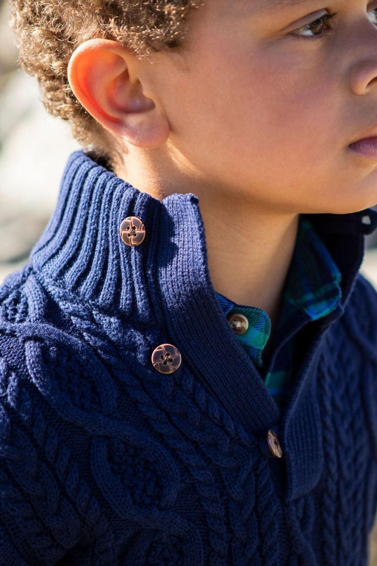 Close-up of a child wearing a navy blue organic cotton sweater with a ribbed mock neck and faux leather buttons.