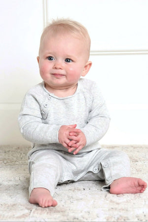 A baby sits on a soft rug, wearing a light gray organic cotton romper with button details and a cozy.