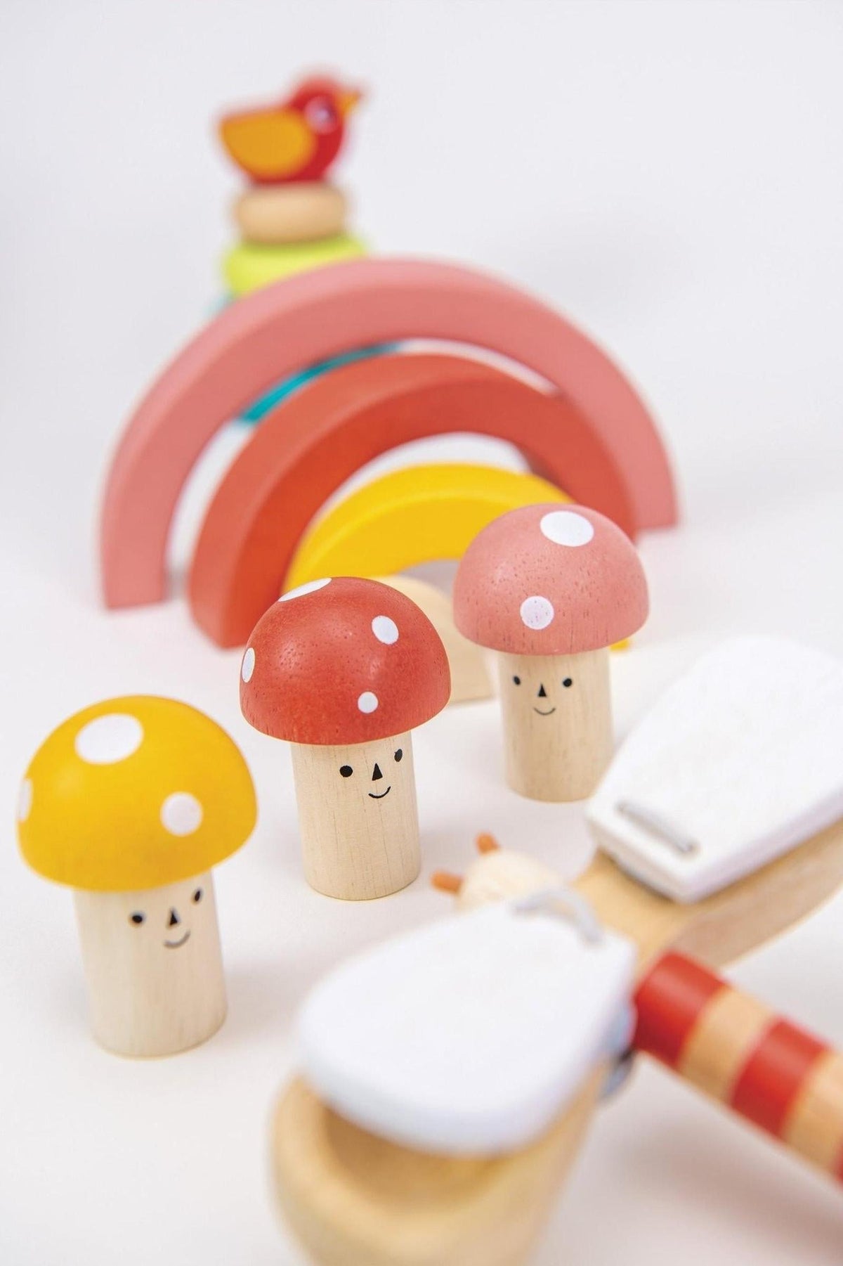 Colorful wooden toy set with smiling mushroom figures and a rainbow arch, featuring eco-friendly materials for toddlers.