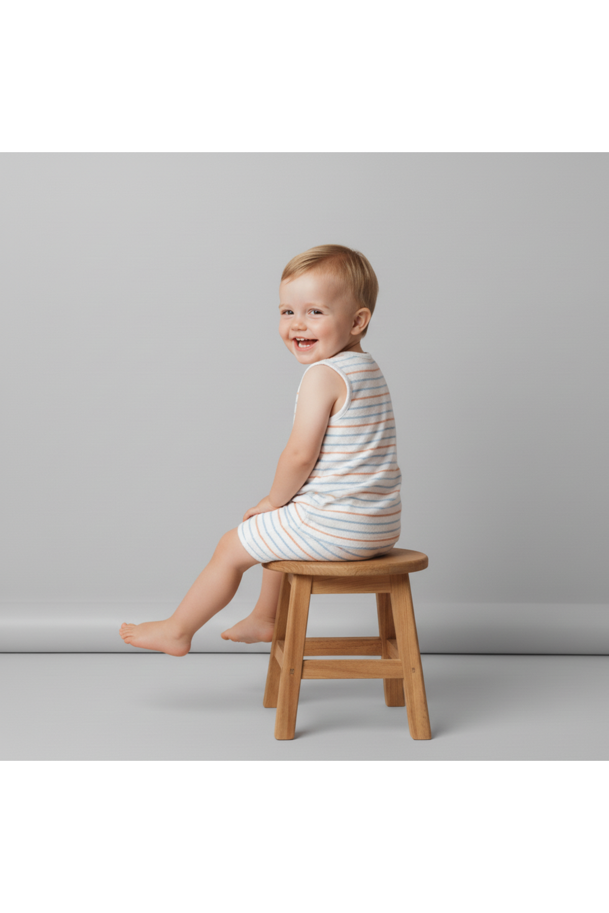 A smiling child sits on a wooden stool, wearing a soft, striped sleeveless tee and shorts set. The outfit features a relaxed fit, ideal for warm weather and play.