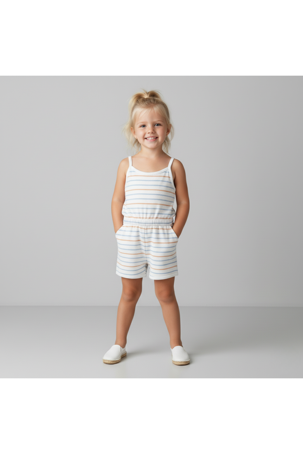 A young girl stands smiling in a soft, breathable tank romper featuring light blue and white stripes. The organic cotton fabric is perfect for warm-weather play and comfort.