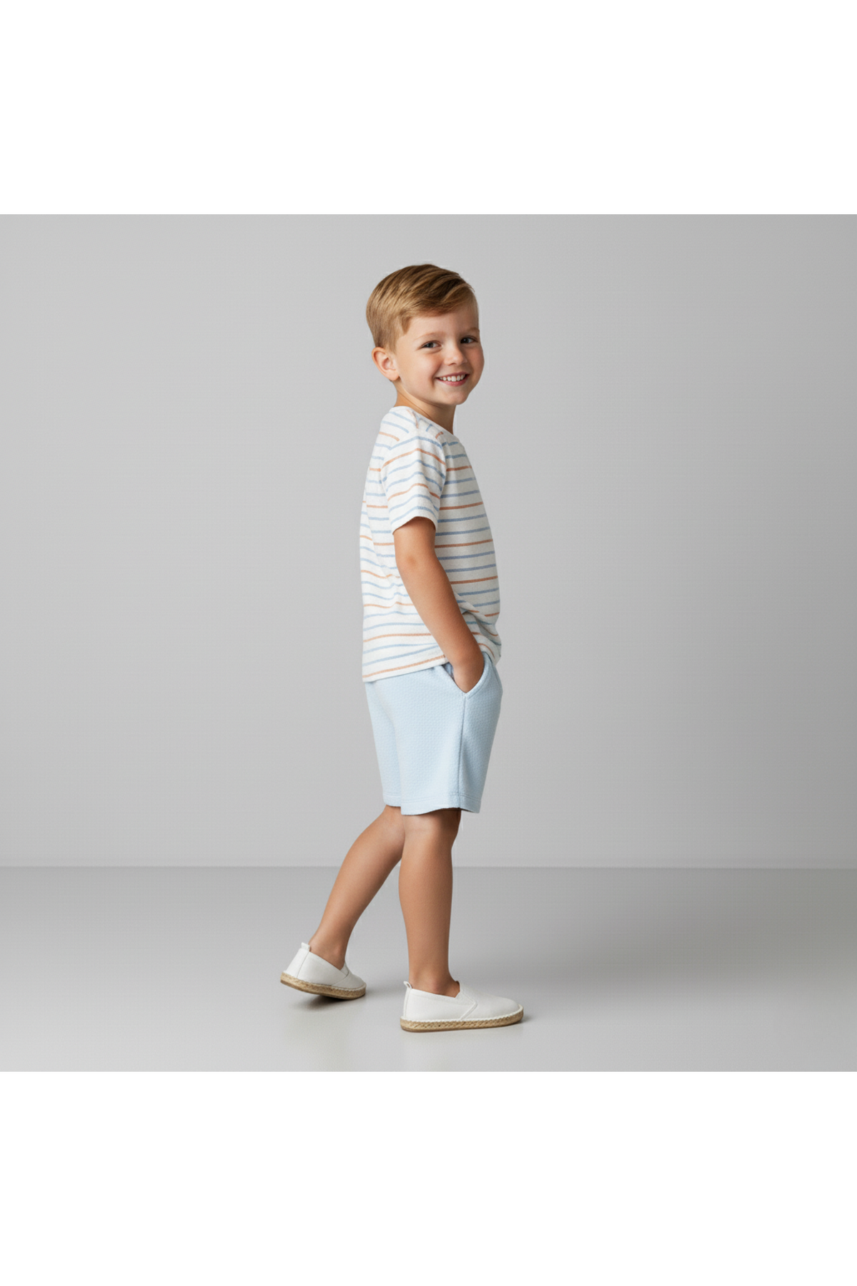 A young child smiles while wearing a striped organic cotton tee and light blue shorts. The outfit features a relaxed fit, perfect for comfortable summer play and casual outings.