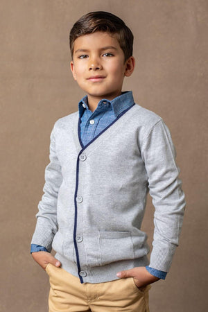 A young boy poses in a grey cardigan with navy tipping, layered over a blue shirt, against a neutral background.