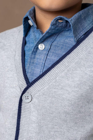 A close-up of a grey cardigan with navy trim, layered over a blue button-up shirt, showcasing soft fabric and stylish.