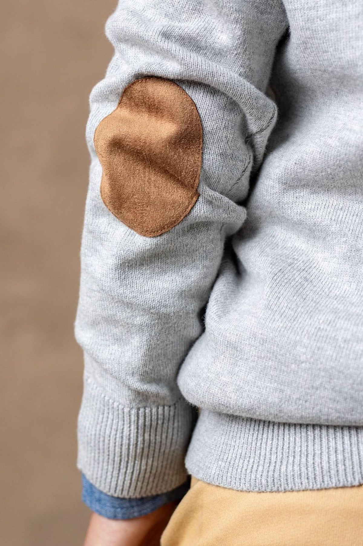 Close-up of a grey organic cotton cardigan featuring a faux suede elbow patch and ribbed cuffs, highlighting its stylish details.