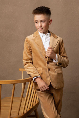 A young boy models a medium brown organic corduroy blazer, featuring button details and a tailored fit, paired with a white shirt.