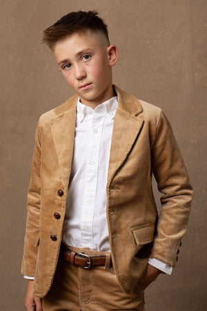 A young boy stands confidently in a medium brown corduroy blazer, featuring button details and a classic cut, paired with a white dress shirt against a neutral backdrop.