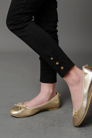 A close-up of a child wearing black ponte pants with button cuffs, paired with shiny gold ballet flats. The outfit highlights a stylish and comfortable look for toddlers and girls.