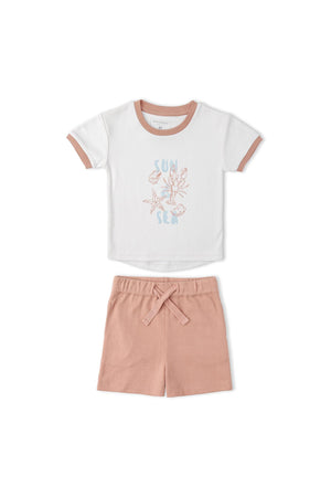 A soft white graphic tee with a Sun print and pink trim is paired with matching pink shorts. The set is made from organic cotton, perfect for comfortable summer wear.