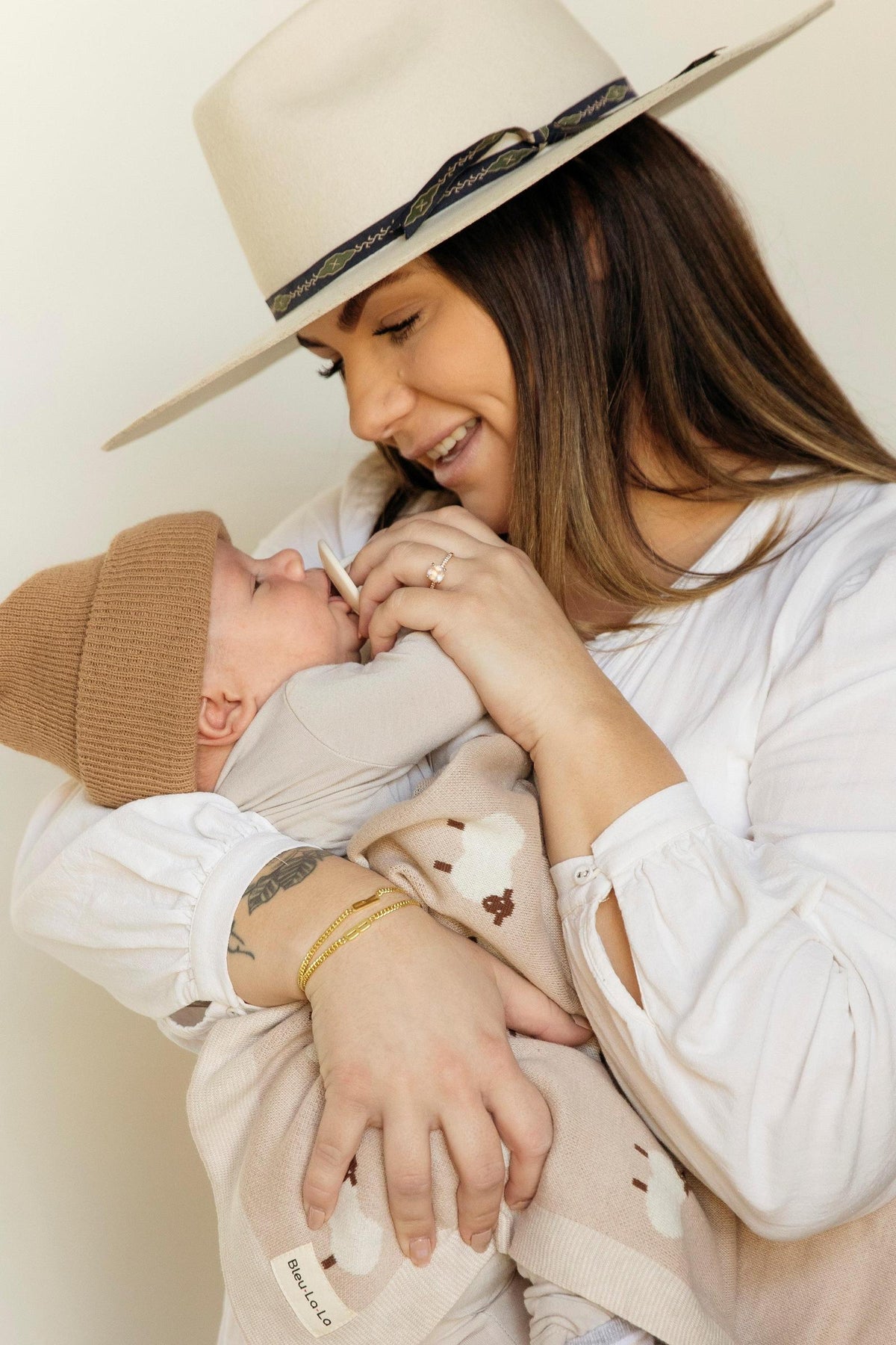 A woman in a white blouse holds a baby wrapped in a sheep-patterned knit blanket, smiling warmly.