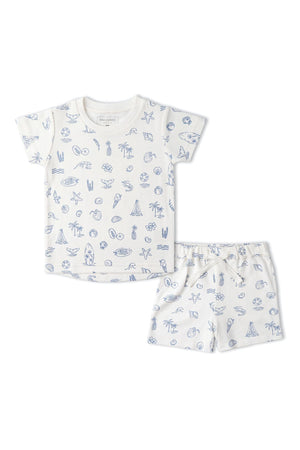 A coastal-themed organic cotton tee and shorts set features playful blue illustrations of seashells, palm trees, and surfboards on a light background. Ideal for summer outings and comfortable play.