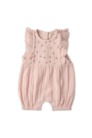 A blush pink organic cotton romper features delicate ruffle accents and intricate floral embroidery. This lightweight, airy garment is perfect for warm-weather days and designed for comfort.