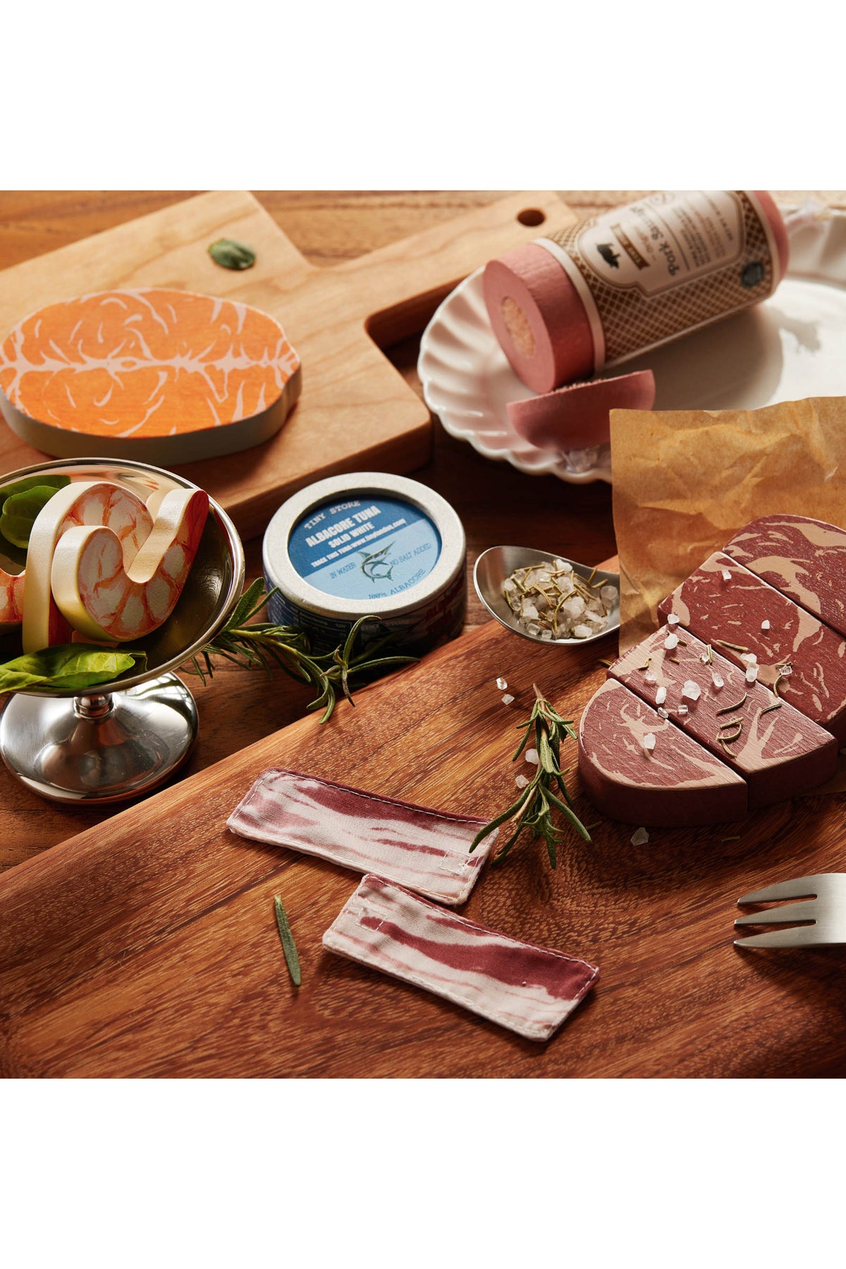 A wooden cutting board displays realistic play food items, including colorful shrimp, steak, and bacon. This organic wooden meat and seafood play food set encourages imaginative cooking adventures for children.