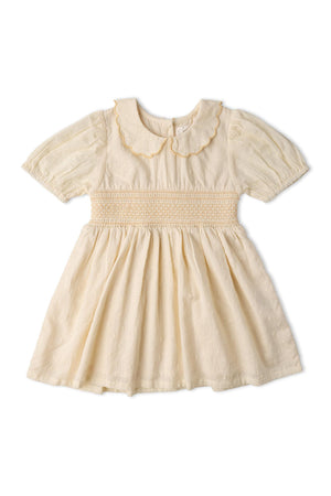 A soft butter yellow dress featuring a smocked collar and puffed sleeves. Made from organic cotton, it has a vintage-inspired design ideal for children’s playdates and special occasions.