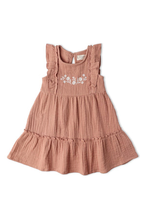 A soft clay-colored tiered dress made of organic muslin cotton features delicate floral embroidery and ruffled straps, perfect for sunny-day adventures. Ideal for little ones who enjoy playful elegance.