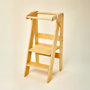 A natural wood foldable educational tower features a sturdy design with two steps and a safety rail, ideal for encouraging children to participate in cooking and other activities alongside adults.