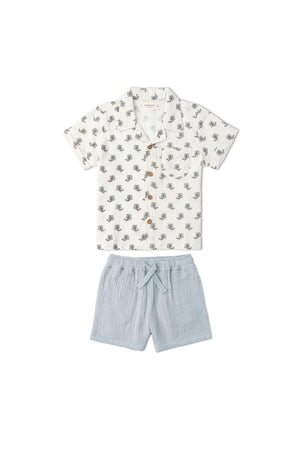 A lightweight, organic cotton shirt and shorts set for children, featuring a white shirt adorned with a subtle green leaf pattern and soft blue shorts, perfect for summer adventures.