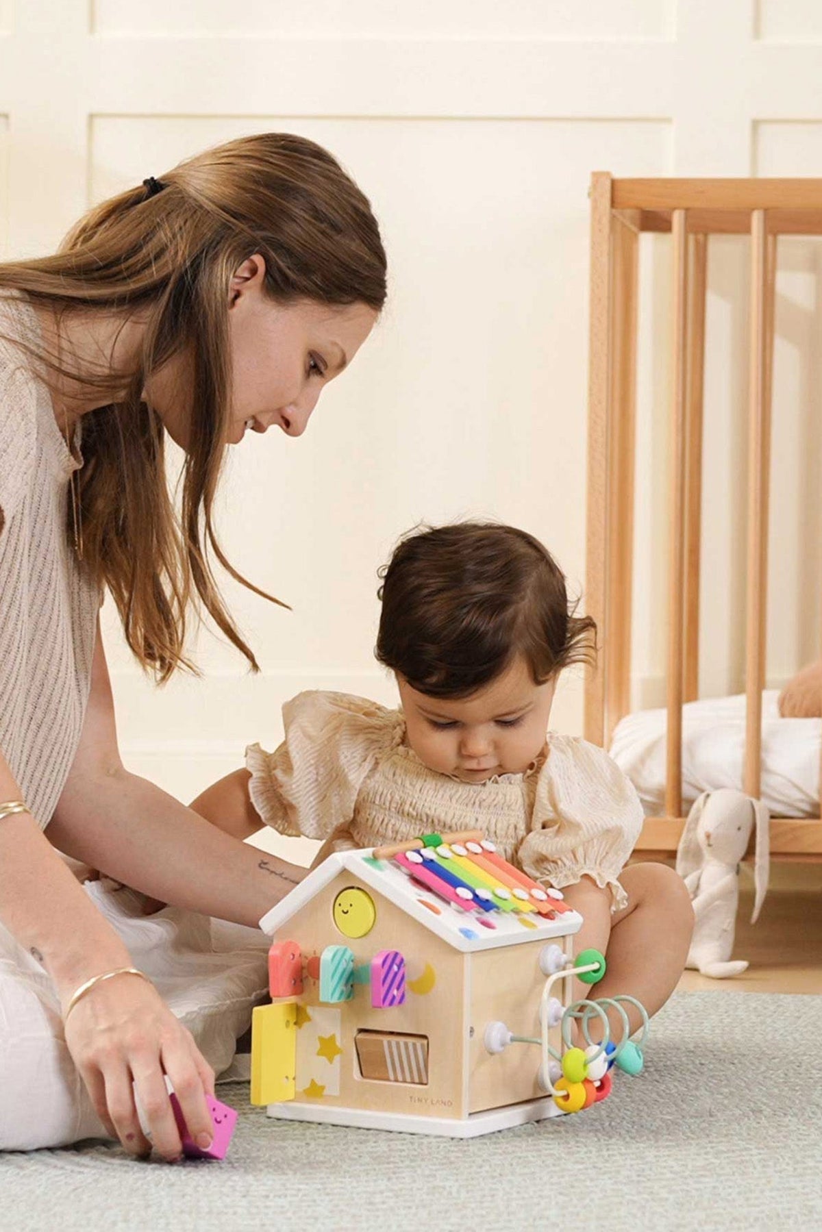 A mother and her toddler engage with a colorful wooden activity cube, promoting exploration and sensory play in a cozy.