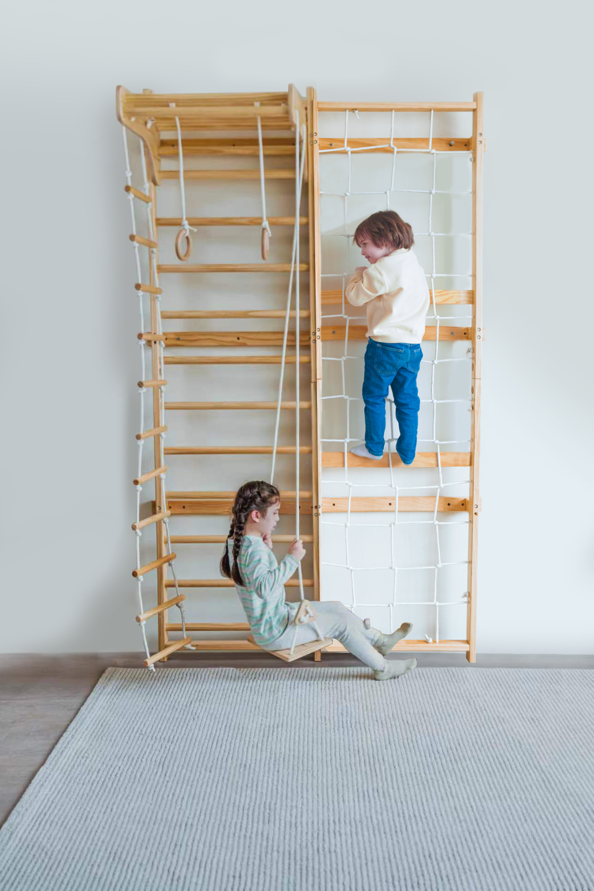 A wooden Swedish wall ladder features a child climbing and another sitting on a swing, both engaged in play indoors.