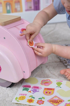 A child decorates a pink wooden scooter with colorful stickers, showcasing the toys interactive and imaginative play features.