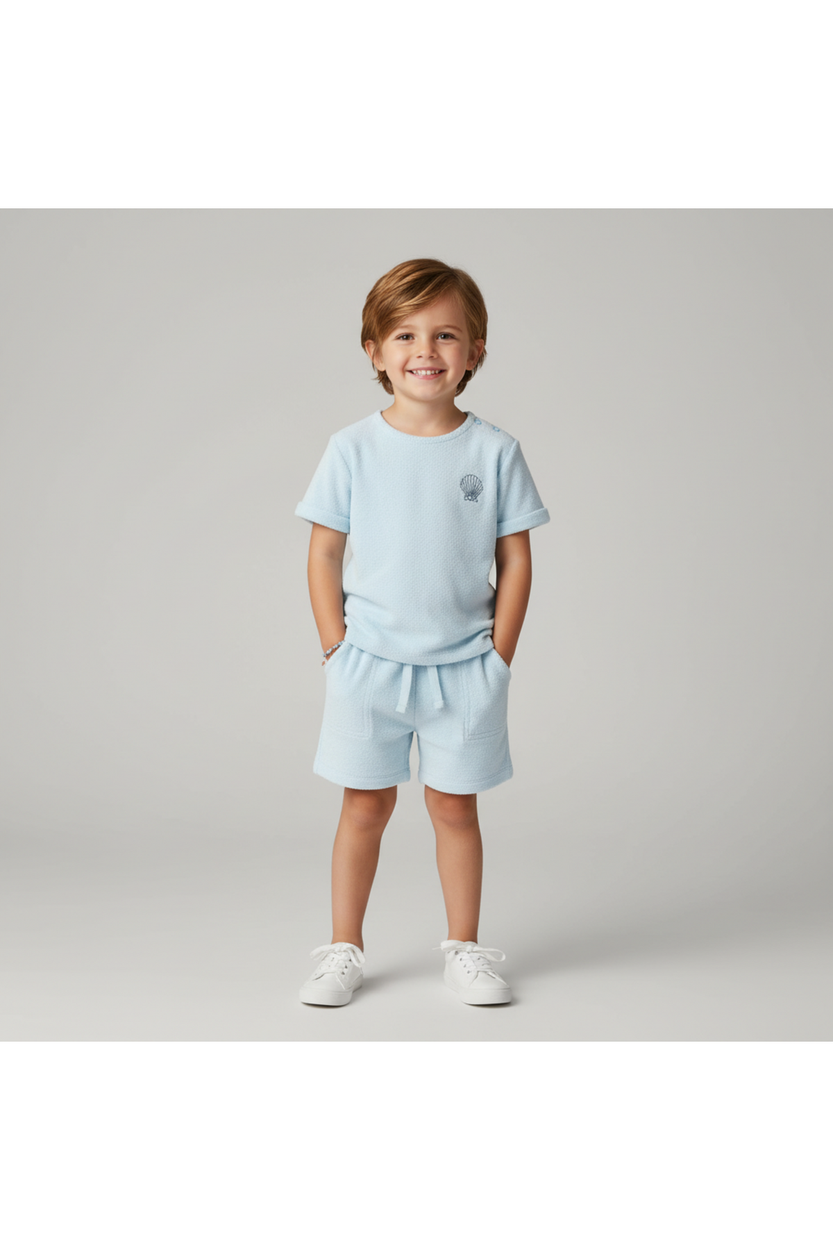 A young child smiles while wearing a light blue organic terry tee and shorts set. The outfit features a relaxed fit and soft, breathable fabric, perfect for summer play and.