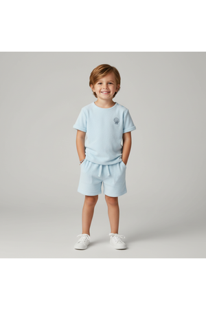 A young child smiles while wearing a light blue organic terry tee and shorts set. The outfit features a relaxed fit and soft, breathable fabric, perfect for summer play and.