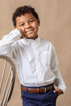 A smiling young boy poses in a white long-sleeve button-down shirt made from organic cotton, featuring a chest pocket.