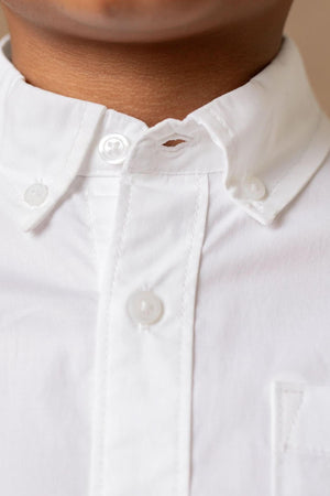 Close-up of a toddler wearing a white button-down shirt made from soft organic cotton poplin. The shirt features a classic collar and a functional chest pocket, highlighting sustainable fashion.