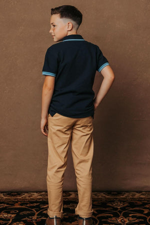 A boy stands with his back to the camera, wearing a navy polo shirt and khaki skinny chinos.