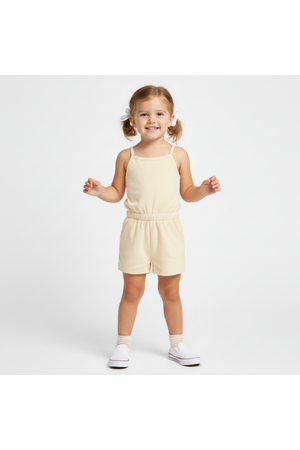 A smiling young girl stands in a light butter yellow organic tank romper, featuring a breathable terry fabric and a relaxed fit, perfect for warm-weather play.