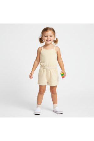 A young girl stands smiling in a light butter yellow tank romper made from soft terry fabric. The outfit features adjustable straps and an elastic waistband, perfect for warm-weather play.