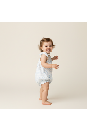 A cheerful toddler with curly hair is wearing a light blue organic cotton bubble romper featuring a delicate floral print.