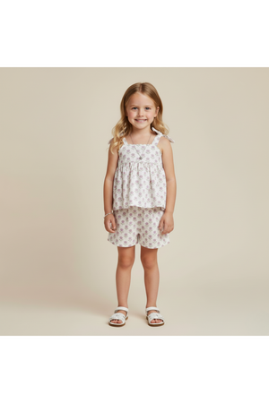 A young girl smiles while wearing a lavender and white organic cotton tie-up top paired with matching shorts. The outfit features a playful floral pattern, perfect for warm-weather outings.