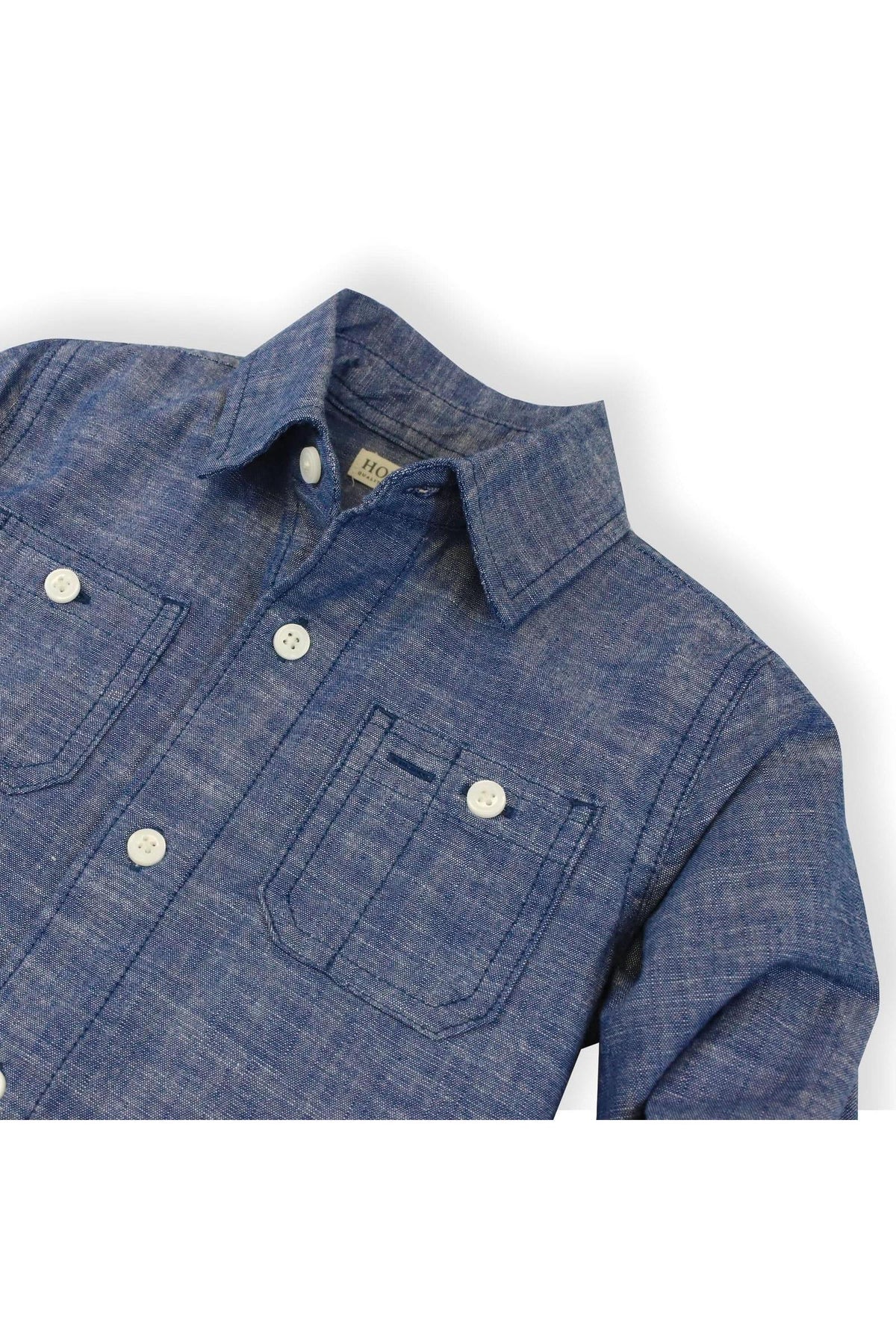Close-up of a blue chambray button-down shirt featuring matte buttons and two chest pockets, made from organic cotton.