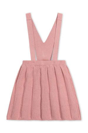 A soft rose-colored overall skirt features pleated detailing and adjustable straps, made from organic cotton for comfort.